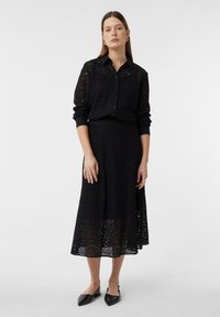 Black lace shirt with button closure and long sleeves, paired with a black lace midi skirt featuring a scalloped hem. Black flats complete the outfit.