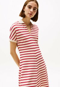 Gestreiftes Polokleid in Rot und Weiß mit V-Ausschnitt und kurzen �Ärmeln. Das Material scheint gestrickt zu sein, hat eine glatte Textur, eine taillierte Passform und seitliche Taschen.