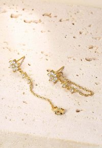 Boucles d'oreilles en or ornées de motifs floraux, agrémentées de pierres précieuses transparentes et de chaînes pendantes, avec un petit accent décoratif à l'extrémité.