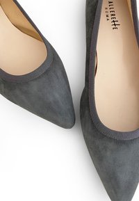 Pump con punta affusolata in suede grigio, con dettaglio di colletto in maglia elastica. Texture liscia e design minimalista. L'interno presenta una fodera in un leggero tono tan.