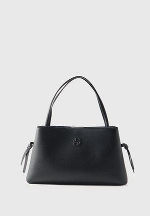 Borsa a mano in pelle nera con doppi manici, logo del marchio discreto al centro e dettagli laterali annodati su sfondo chiaro uniforme.