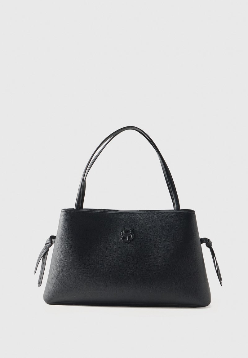 Sac à main en cuir noir avec doubles anses, logo de marque discret centré et détails noués sur les côtés sur un fond clair uni.