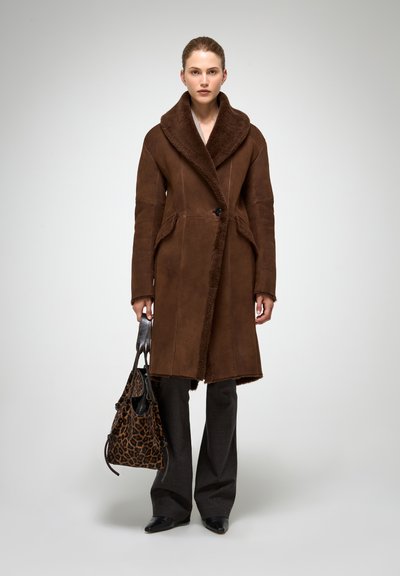 Pruun shearling-voodriga mantel, laia kraega, nööpidega kinnitusega ja küljetaskutega. Kombineeritud tumedate pükste ja leopardimustrilise kotiga.