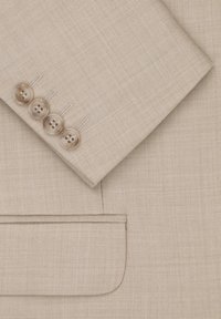 Beżowa marynarka z tkaniny o teksturowanym splocie. Cztery zaokrąglone guziki na mankiecie z delikatnym połyskiem. Kieszeń z kontrastowym wykończeniem szwem.