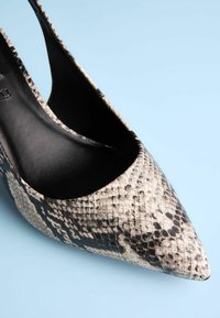Spitz zulaufender High Heel mit einem schwarz-creamfarbenen Schlangenprint-Muster, ausgestattet mit einem Innenfutter aus schwarzem Leder und einem Slingback-Design.