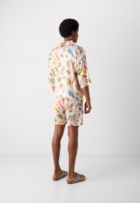 Conjunto de camisa de manga corta y pantalones cortos en rosa claro con patrones tropicales coloridos. El material parece suave y tiene un corte relajado.