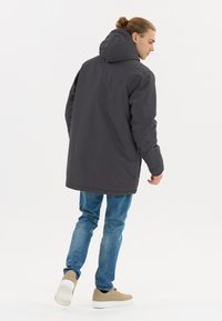 Grå huvad jacka i texturerad tyg, med lös passform och rak snitt, kombinerad med ljusblå jeans och beige sneakers.