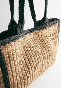 Geweven tan kleurige strooien draagtas met zwarte gevlochten hante. Kenmerkt zich door een gestructureerd oppervlak met verticale strepen en een contrasterende rand.