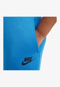 Siniset puuvillashortsit, joissa on sivutasku ja musta Nike-logo vasemmassa alakulmassa. Sileä pinta ja rento muotoilu.