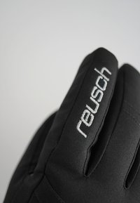 Schwarze gepolsterte Handschuhe mit weicher Textur. Gesticktes "reusch"-Logo in Silber im Bereich des Handgelenks. Strapazierfähiges Material, das für kaltes Wetter konzipiert ist.