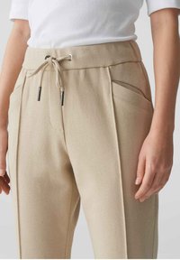 Beige op maat gemaakte broeken met een elastische taille met trekkoord, zilverkleurige hardware en zijzakken. Gestructureerde stof met een gladde afwerking.