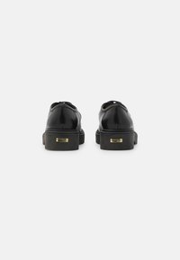 Zwarte leren schoenen met een strak ontwerp, voorzien van een ronde neus en platte zool. Gouden hardware-accenten op de hak voegen detail toe.