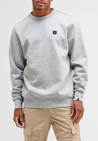 Grijze sweatshirt met een ronde hals, ribgebreide manchetten en zoom, en een klein zwart logo op de borst. Zacht, textuur stof.