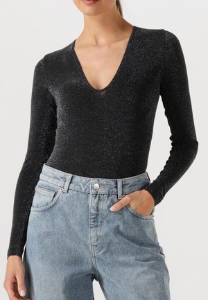 Body noir à manches longues avec un col en V profond, fabriqué en tissu texturé et scintillant, associé à un jean en denim bleu clair taille haute.