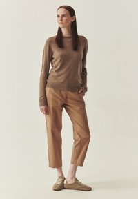 Pull en tricot marron, pantalon court couleur sable et baskets en daim brun clair. Texture douce, design simple et coupe décontractée.