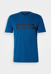 Camiseta de algodón azul con un gran logo negro "BOSS" en el pecho. Cuello redondo clásico y mangas cortas. Textura suave.