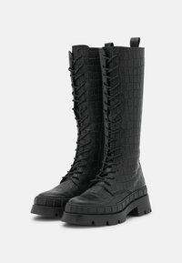 Bottes montantes noires à texture crocodile, avec lacets et semelle en caoutchouc épaisse pour un soutien et une traction accrus.