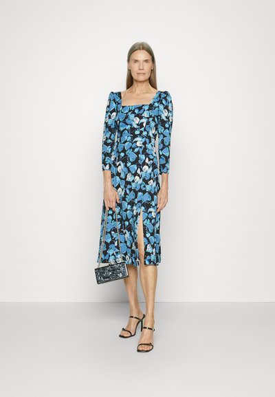 Φλοράλ μίντι φόρεμα σε μαύρο και μπλε χρώμα με μακριά μανίκια, τετράγωνη λαιμόκοψη και μπροστινό σκίσιμο. Συνδυασμένο με μια μικρή μαύρη τσάντα και σандάλια με λουράκια.