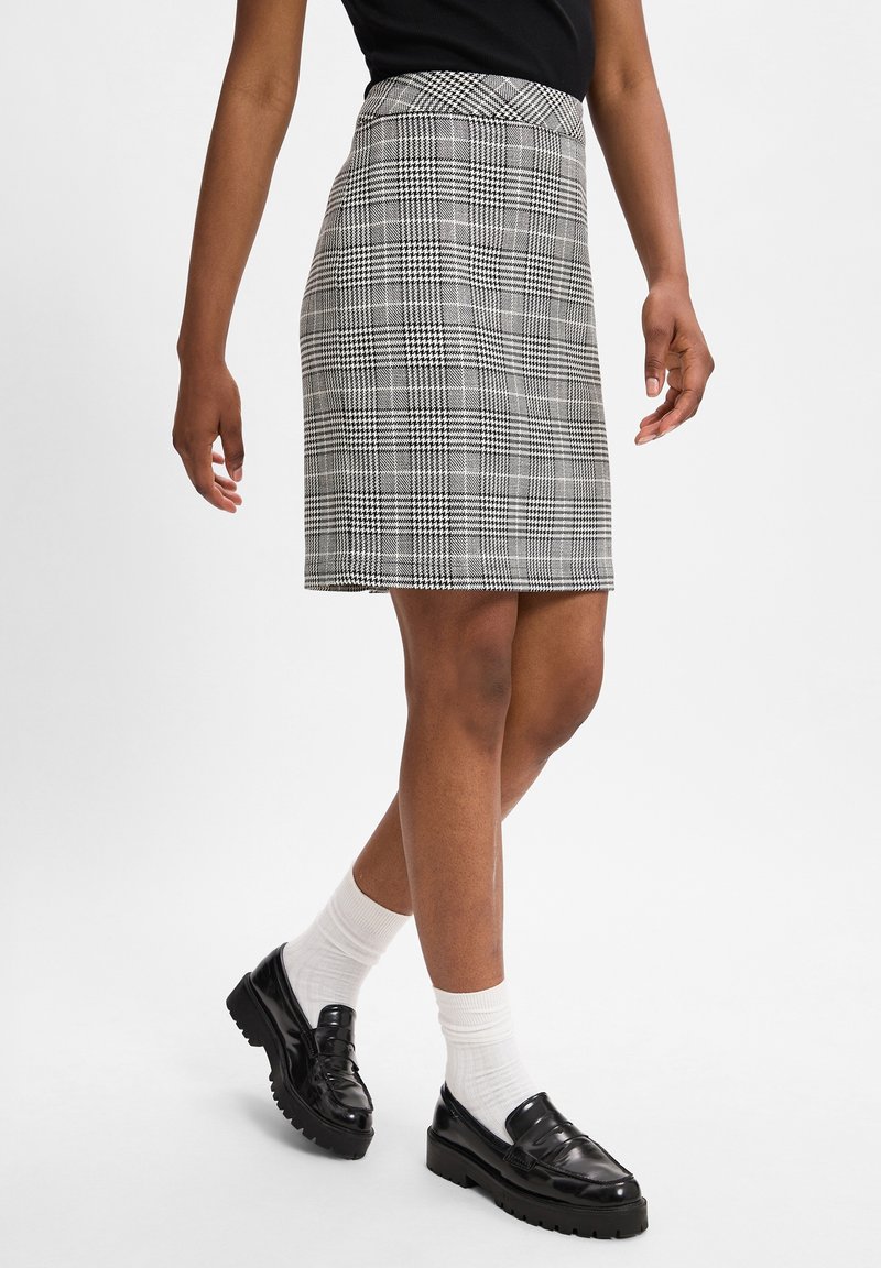 Jupe à carreaux noir et blanc avec une taille cintrée, d'une coupe à mi-genou et d'une texture lisse, associée à des mocassins noirs et des chaussettes blanches.