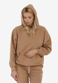 Beżowy, oversize'owy hoodie z przednią kieszenią, regulowanym kapturem na sznurku i miękką teksturą, w zestawie z dopasowanymi spodniami dresowymi.
