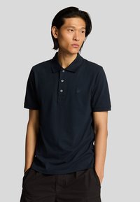 Polo de color navy hecho de algodón con un cuello, tapeta de tres botones y un pequeño logo bordado en el lado izquierdo del pecho. Textura suave.