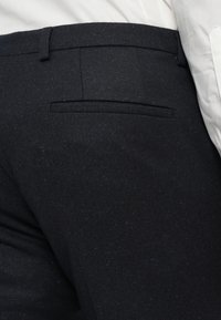 Σκοτεινές υφασμάτινες παντελόνες με υφαντή υφή και πιτσιλιές μπλε και καφέ, σχεδιασμένες με μία πίσω τσέπη και θηλιές ζώνης.