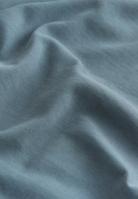 Material moale, texturat, de culoare albastru deschis, cu un aspect ușor zbârcit și un model fin de tricotaj pe toată suprafața.