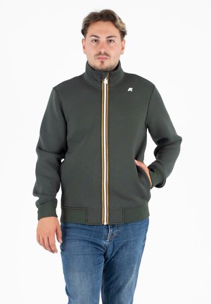 Donkergroen zip-up jack met hoge kraag, witte en oranje verticale rits en voorzakken. Gladde textuur en nauwsluitend ontwerp.
