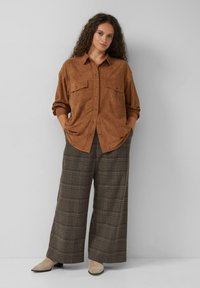 Bruine suèdeachtige shirt met knoopsluitingen en twee borstzakken, gecombineerd met wijduitlopende geruite broek in bruine en beige tinten.