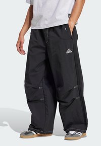 Melnas, brīva piegriezuma bikses ar teksturētu apdari, ar baltu akcentu šuvēm un izšūtu Adidas logo. Sānu rāvējslēdzis regulēšanai.