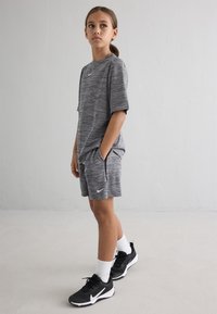 Γκρι αθλητικό μπλουζάκι και σορτσάκι με υφή, λευκό λογότυπο Nike, συνδυασμένα με μαύρα αθλητικά παπούτσια και λευκές κάλτσες, παρουσιασμένα σε ανοιχτό φόντο.