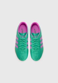 Zelene športne čevlje s poudarki v roza barvi in tremi črtami, z zgornjim delom iz semiša in teksturiranim notranjim podlogom. Klasična zasnova z vezalkami.
