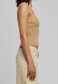 Top tan a costine, senza maniche, con un alto colletto e una vestibilità aderente. Abbinato a pantaloni chiari con una tasca visibile e cerniera.
