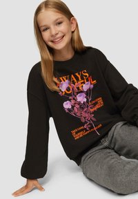 Sweatshirt noir avec graphique floral coloré et texte. Matériau doux, coupe oversize, manches larges, associé à un jean gris.