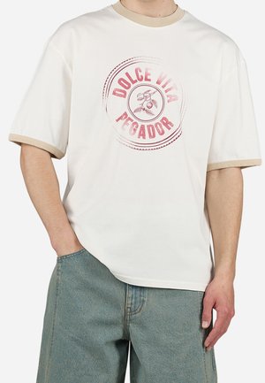 White t-shirt with beige accents, short sleeves, and a round graphic design featuring "DOLCE VITA PEGADOR" in a vintage style.