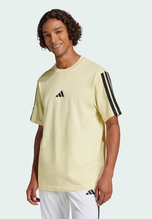 Camiseta de algodón amarillo claro con mangas cortas, con el logo de adidas en negro y tres franjas negras en cada hombro.