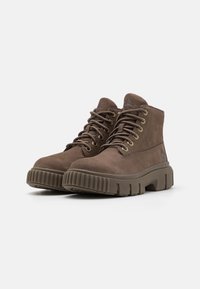 Stivaletti in suede marrone con punta tonda, chiusura con lacci, occhielli in metallo e suola in gomma rigata. Presenta un dettaglio con logo sul lato.
