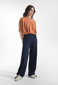 Pomarańczowa oversize koszulka wykonana z miękkiego materiału, zestawiona z granatowymi spodniami o szerokich nogawkach z kieszeniami, stylizowana z jasnymi sneakersami.