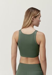 Olivgrön sportbehå med en åtsittande design, tillverkad av ett glatt tyg, med racerback-stil och en kontrasterande ljus kant längs kanterna.