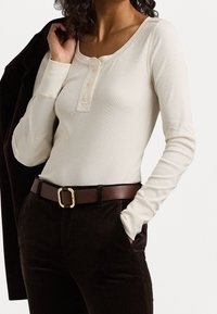 Długi rękaw kremowy top w prążki z okrągłym dekoltem i trzema guzikami, zestawiony z ciemnobrązowymi spodniami z korduroy i brązowym paskiem.