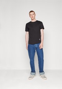 Black cotton t-shirt with short sleeves and a crew neckline, paired with light blue denim jeans and grey sneakers with white accents.