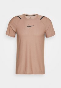 Camiseta Nike Dri-FIT en tono marrón claro, con cuello redondo, mangas cortas y un logo Swoosh negro en el pecho, complementado con acentos negros en los hombros.