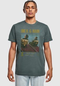 Grafisk t-shirt i mørkegrå med et falmet print af to figurer på forsiden, med guldtekst og forskellige farvede designelementer.