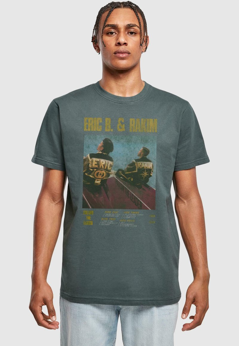 Grafisk t-shirt i mørkegrå med et falmet print af to figurer på forsiden, med guldtekst og forskellige farvede designelementer.