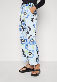 Floral-patterned, light blue trousers with a relaxed fit, elastic waistband, and side pockets, paired with black platform sandals.