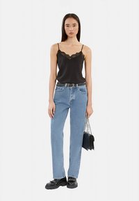 Svart satinlinne med spetskant, kombinerat med ljusblå högmidjade raka jeans och svarta platåskor, håller i en handväska.