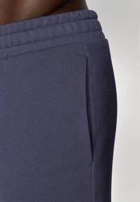 Calças de treino azul-marinho feitas de um tecido suave e texturizado, com um cós elástico e um bolso lateral para armazenamento.
