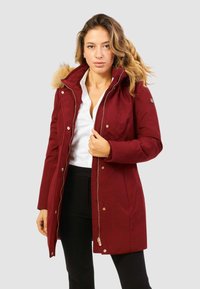 Parka rossa con cappuccio foderato in pelliccia sintetica, chiusura con zip e bottoni automatici. Presenta un design aderente e un tessuto morbido e testurizzato.