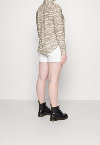 Tansrandig skjorta med knappar, vita shorts och svarta snörkängor med gula detaljer. Fokusera på tygmönster och former.