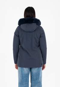 Giacca invernale blu navy con cappuccio foderato in pelliccia, progettata con una forma aderente. Materiale esterno liscio, caratterizzato da uno stile pulito e minimalista.